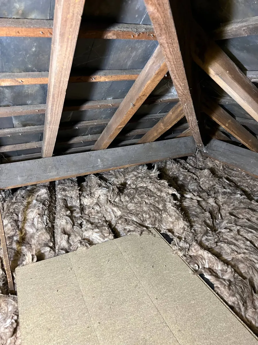 Old, flattened loose wool insulation between loft joists, with a few boards laid over it